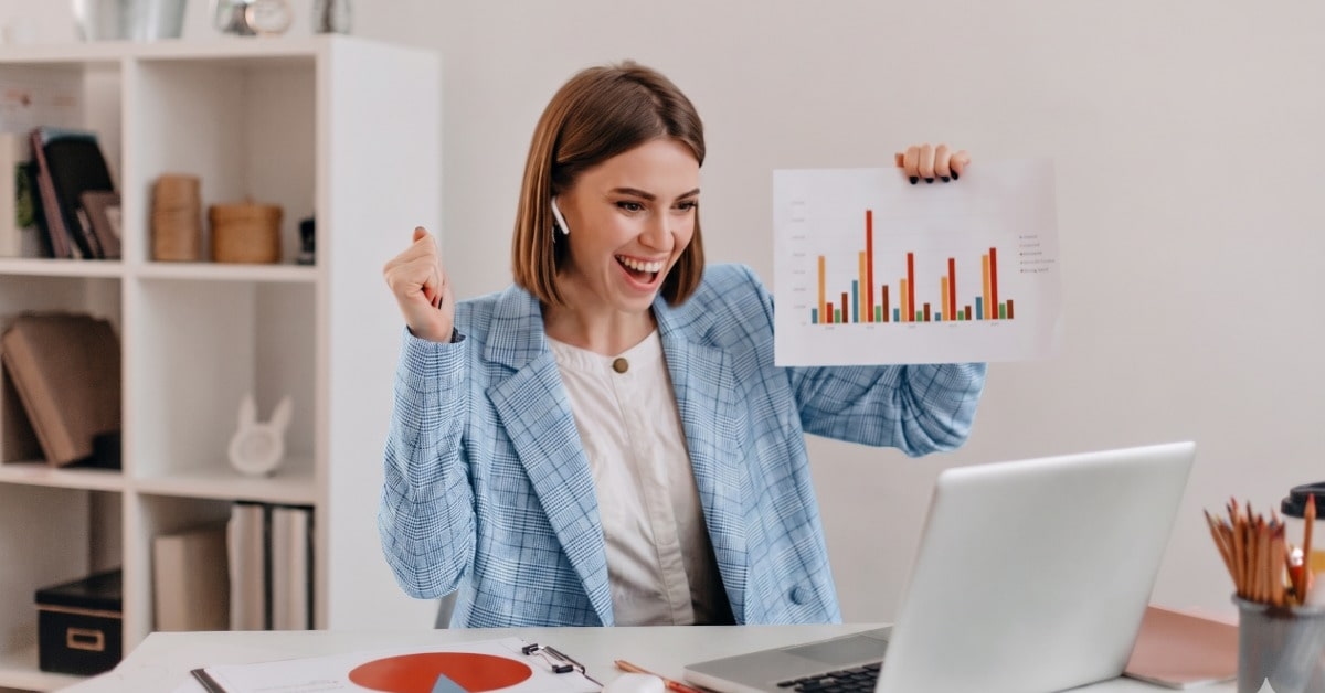 Mulher comemora resultados em frente ao computador após aprender como alavancar as vendas
