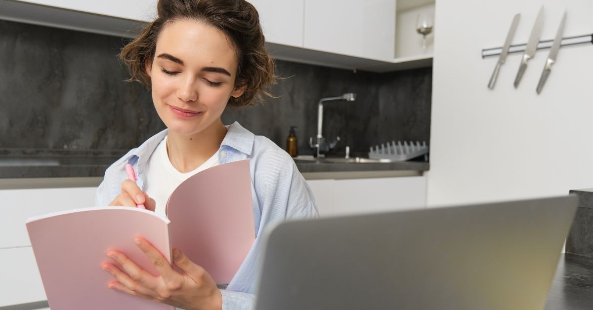 Mulher anotando ideias de nomes para loja de roupas em um caderno em frente ao notebook