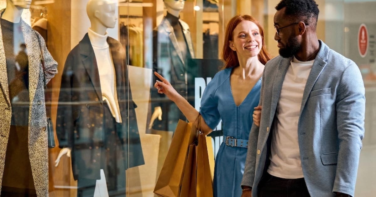 Casal de mulher e homem passam em frente a uma vitrine de loja após lerem frases para atrair clientes